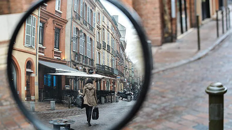 close up image of a vehicle's rearview mirror reflecting a street lined with buildngs