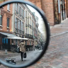close up image of a vehicle's rearview mirror reflecting a street lined with buildngs